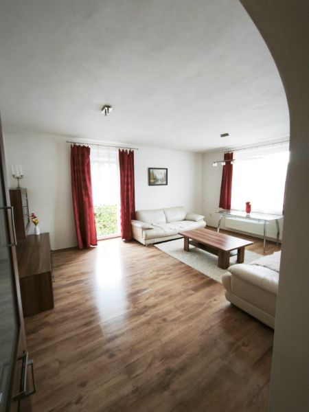 Wohnzimmer eines Einfamilienhauses mit Holzboden, weißen Möbeln und roten Vorhängen.