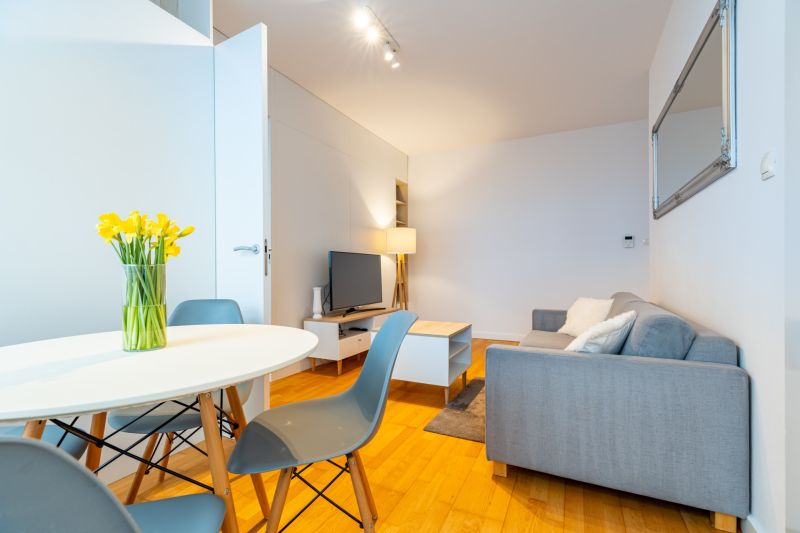Wohnzimmer mit Holzboden, grauem Sofa und Esstisch in einer Zweizimmerwohnung.