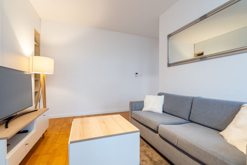Graues Sofa mit Kissen im Wohnzimmer, Holzboden, großer Spiegel.