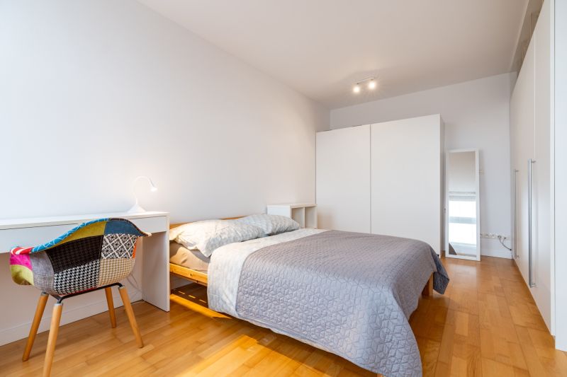 Schlafzimmer in einer 2-Zimmer-Wohnung mit Bett, Schreibtisch und Boden mit Holzdekor.