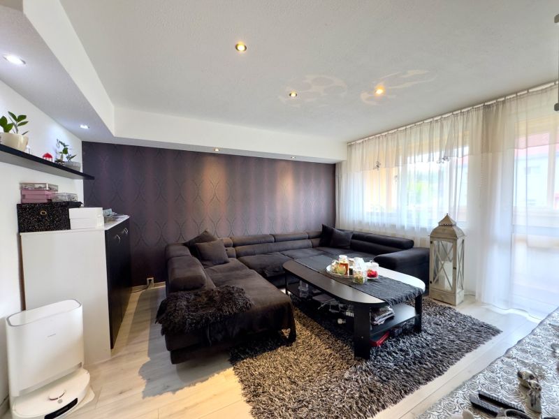 Wohnzimmer in einer 4-Zimmer-Wohnung mit einem dunklen Sofa, einem Boden mit Holzdekor und Dekorationen.