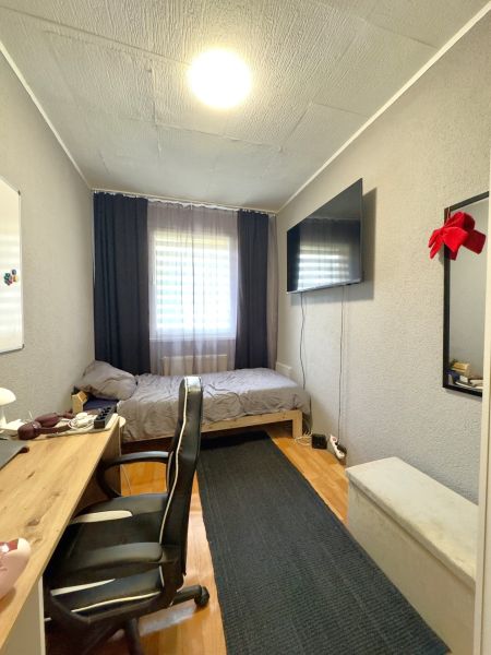 Ein Zimmer in einer 4-Zimmer-Wohnung mit einem Schreibtisch, einem Bett und einem Fernseher an der Wand.