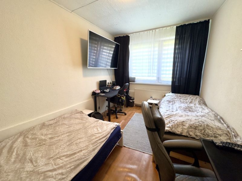 Ein Zimmer in einer 4-Zimmer-Wohnung mit zwei Betten, Holzboden und einem Schreibtisch.