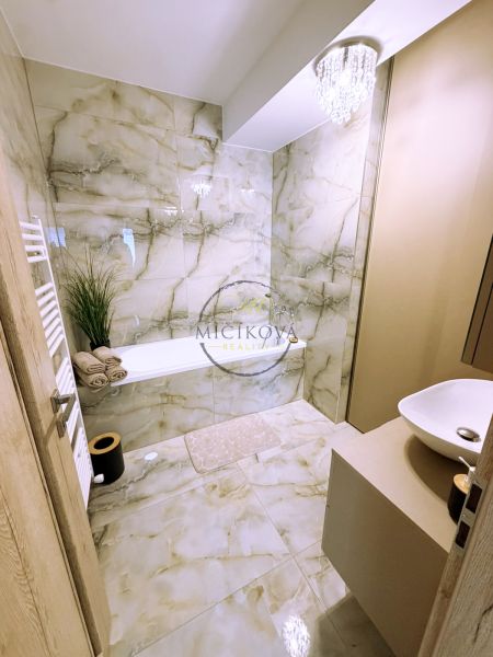 Badezimmer mit Badewanne, Kronleuchter und Marmorverkleidung in einer 2-Zimmer-Wohnung.