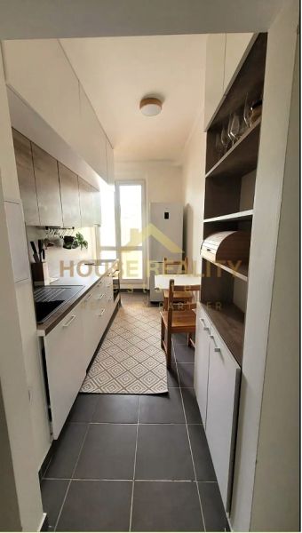 Eine schmale Küche in einer 3-Zimmer-Wohnung mit weißen Schränken und dunklem Boden.