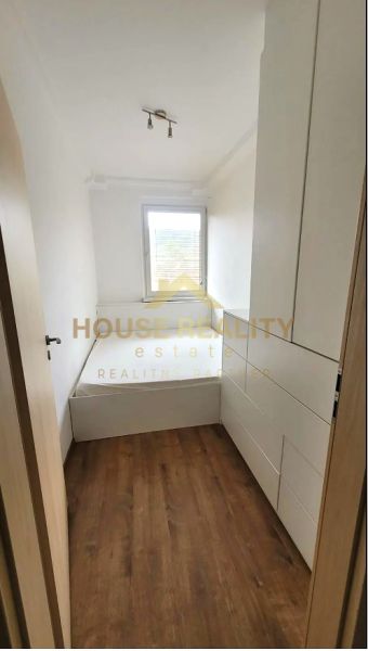 Ein schmales Zimmer mit einem Bett und Einbauschränken, Boden mit Holzdekor.