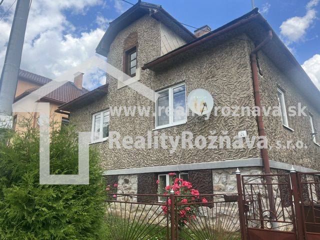 Ein Einfamilienhaus in Rudná mit einer strukturierten Fassade, einem grünen Zaun und Blumen im Garten.