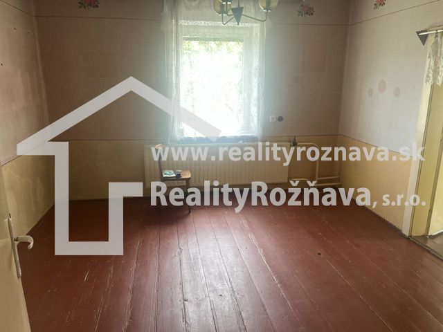 Ein Zimmer in einem Einfamilienhaus mit Holzboden, Wände in Pastellfarben, Fenster mit weißem Vorhang.