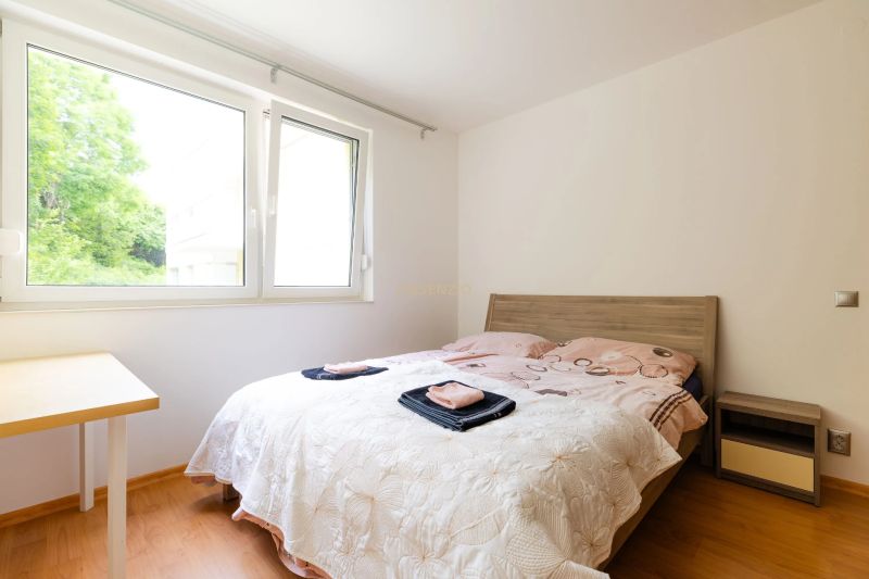 Schlafzimmer in einer 2-Zimmer-Wohnung mit Fenster, Bett und Boden in Holzoptik.
