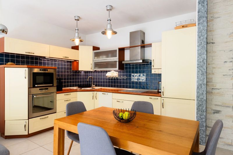 Küche in einer 2-Zimmer-Wohnung mit Holztisch, blauen Fliesen und hellen Schränken.
