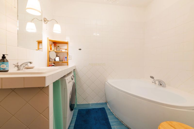 Badezimmer mit Badewanne, Waschmaschine, blauem Teppich und weißen Fliesen in einer 2-Zimmer-Wohnung.