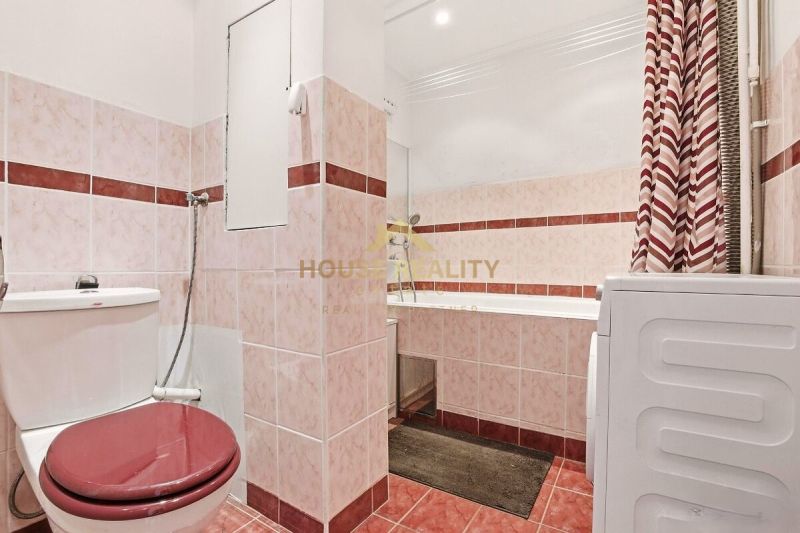 Badezimmer in einer 2-Zimmer-Wohnung mit Dusche, Badewanne und Waschmaschine, dominiert von roten Fliesen.