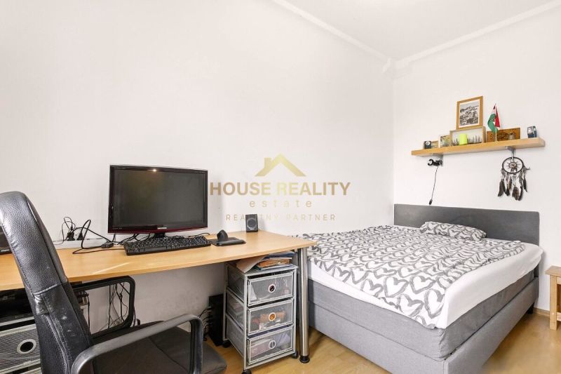 Schlafzimmer in einer 2-Zimmer-Wohnung mit Bett, Tisch und Boden in Holzoptik.
