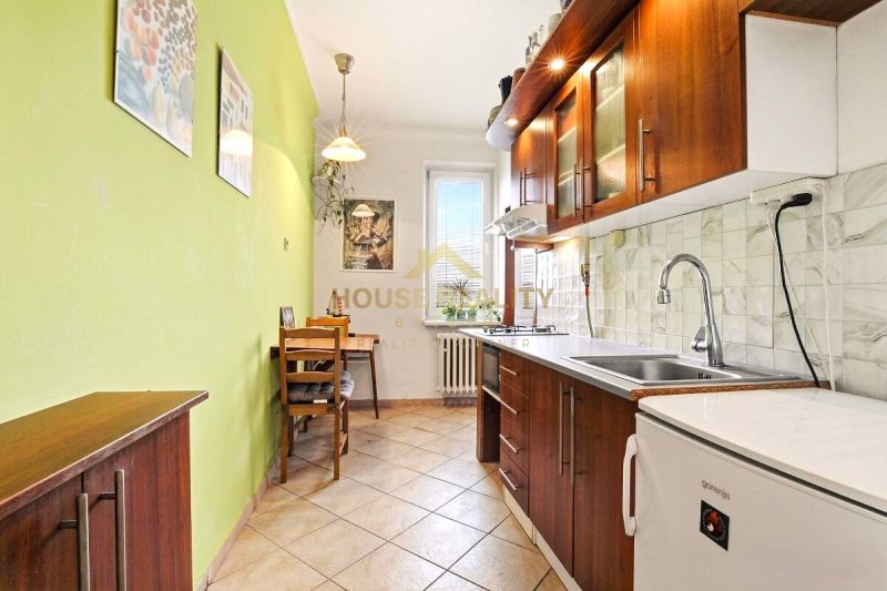 Küche in einer 2-Zimmer-Wohnung mit Holzdekor und grüner Wand, Sitzgelegenheit am Tisch.