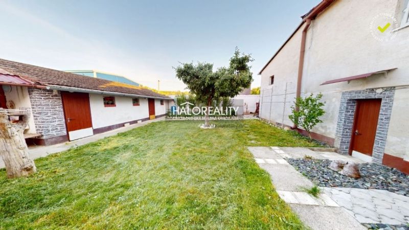Der Garten eines Einfamilienhauses in Senica mit Rasen, einem Baum und zwei Gebäuden.