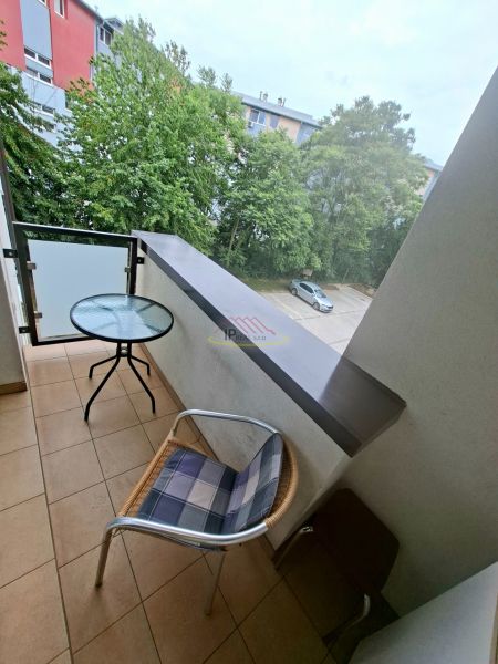 Balkon eines Einzimmerapartments mit Blick auf Grünflächen und einen Parkplatz, Raum mit Tisch und Stuhl.