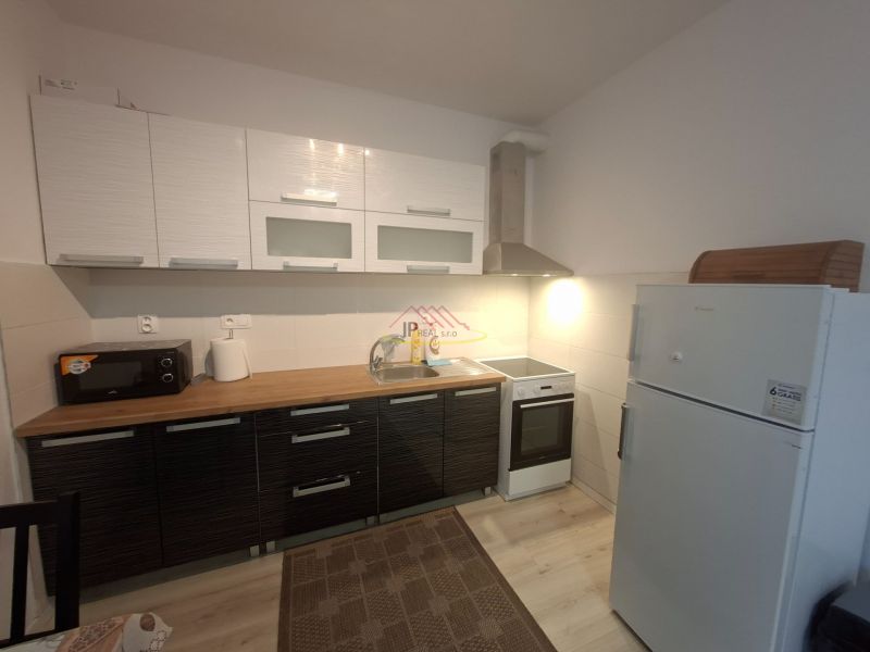Küche in einem Einzimmerapartment mit Küchenzeile, Mikrowelle, Spüle und Kühlschrank, Boden mit Holzdekor.