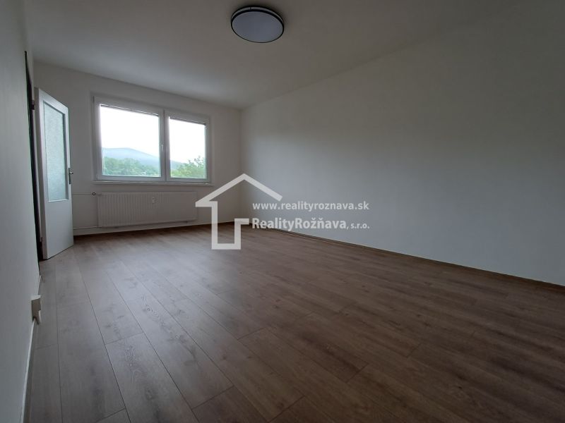 Ein Zimmer in einer 3-Zimmer-Wohnung mit einem Boden in Holzoptik, einem großen Fenster und einem Heizkörper.
