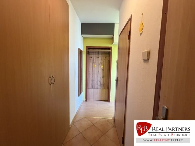Flur mit Schrank und Garderobe in einer Einzimmerwohnung mit Fliesen und Holzmuster.