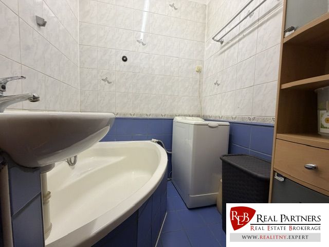 Badezimmer in einer Einzimmerwohnung mit Badewanne und Waschmaschine, gefliest mit weißen und blauen Fliesen.