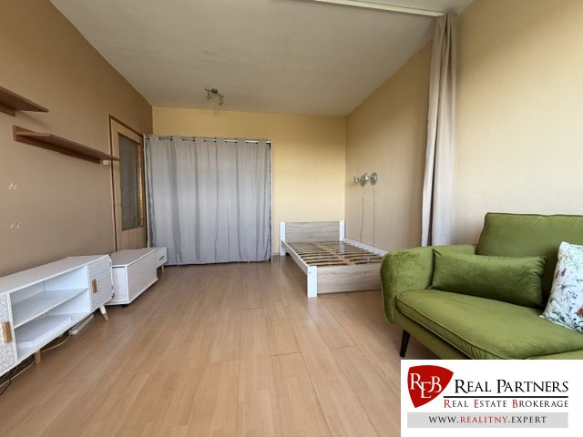 Ein Zimmer in einer Einzimmerwohnung mit Holzboden, einem Bett und einem grünen Sofa.