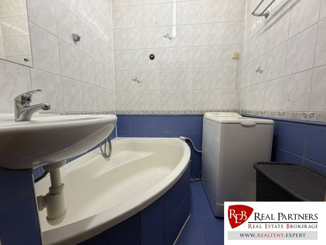 Badezimmer in einer Einzimmerwohnung mit Dusche, Waschbecken, Waschmaschine und blauen Fliesen.