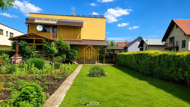 Garten und Einfamilienhaus in Slovenská Ľupča mit gepflegtem Rasen und Blumenbeeten.