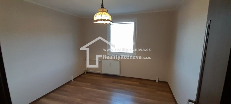 Ein Zimmer in einer 2-Zimmer-Wohnung mit einem Boden in Holzdekor und einer Lampe über dem Heizkörper.