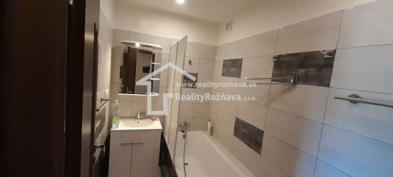 Badezimmer mit Badewanne und Waschbecken in einer Zweizimmerwohnung, gefliest mit hellen Fliesen.