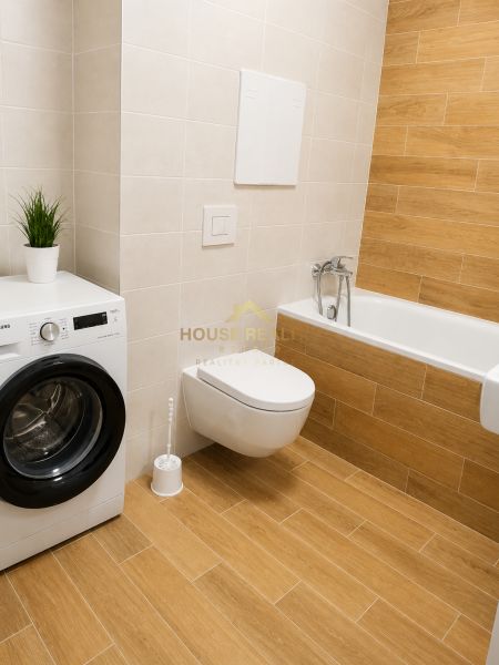 Badezimmer mit Toilette, Badewanne, Waschmaschine und Holzboden in einer Einzimmerwohnung.
