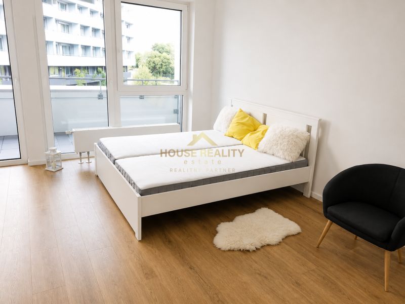 Einzimmerwohnung mit Bett, Sessel, Holzboden und Balkontüren.