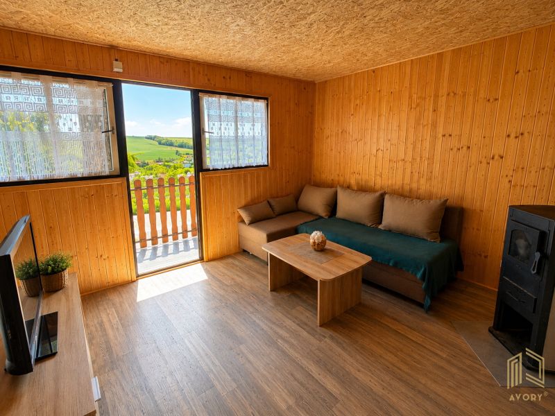 Wohnzimmer in einer Hütte mit Sofa, Fernseher und Holzboden, Blick auf die Landschaft.