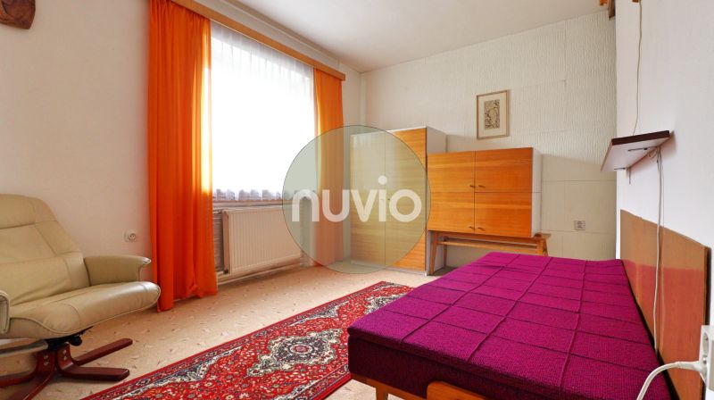 Ein Zimmer in einem Einfamilienhaus mit einem hellen Sessel, Möbeln und auffälligen orangefarbenen Vorhängen.