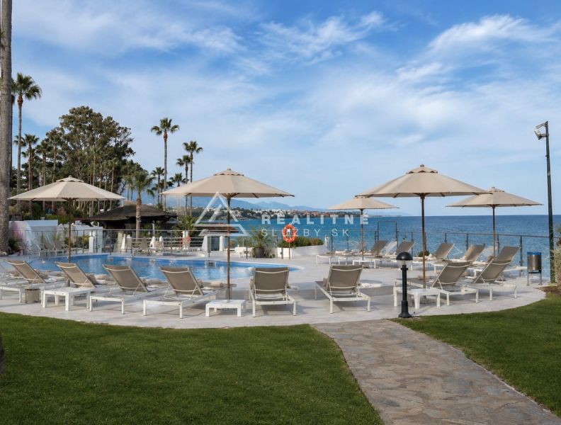 Ein Pool mit Liegestühlen und Palmen am Strand von Dominion Beach in Estepona.
