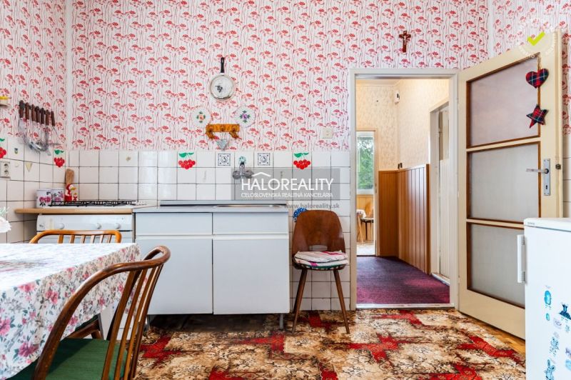 Küche in einem Einfamilienhaus mit Retro-Tapete, weißen Schränken und gemustertem Teppich.