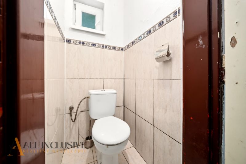 Kleines Badezimmer mit Toilette, gefliest mit hellen Fliesen, mit Fenster und Papierhalter.