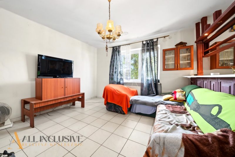 Wohnzimmer mit Fernseher, Sofa und Schrank in einem Einfamilienhaus, Licht durch Vorhänge.