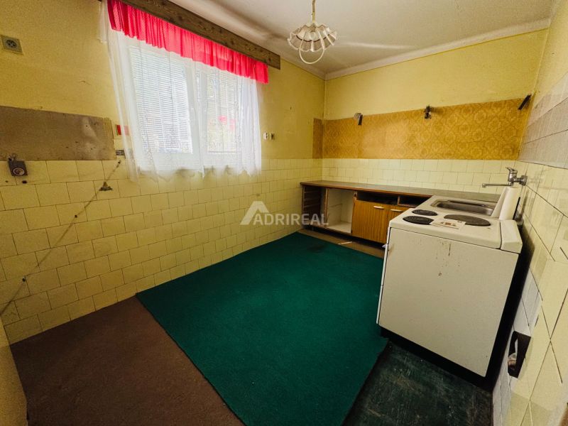 Küche in einer 2-Zimmer-Wohnung mit Linoleumboden und einem Fenster mit Vorhängen.