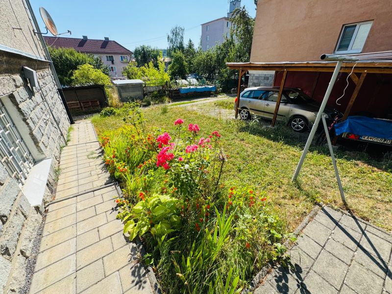 Blumenbeete an der Straße in Krupina, neben einer 2-Zimmer-Wohnung, Auto unter einem Unterstand geparkt.