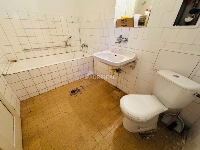 Badezimmer in einer 2-Zimmer-Wohnung mit Badewanne, Waschbecken und Toilette, gefliest mit weißen Fliesen.