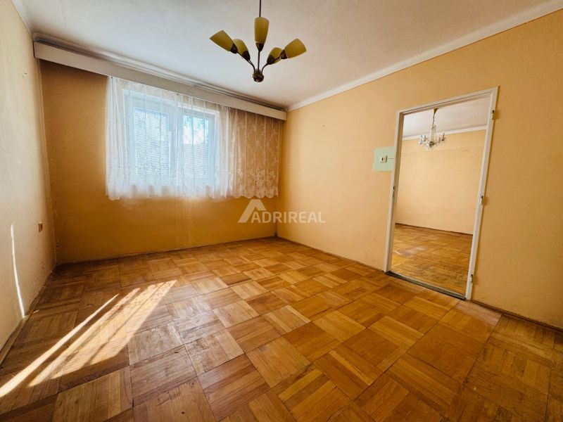 Ein Zimmer in einer 2-Zimmer-Wohnung mit einem Boden in Holzoptik und Vorhängen am Fenster.