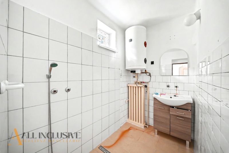 Badezimmer im Einfamilienhaus mit Fliesen, Dusche, Boiler und Waschbecken mit Holzmaske.