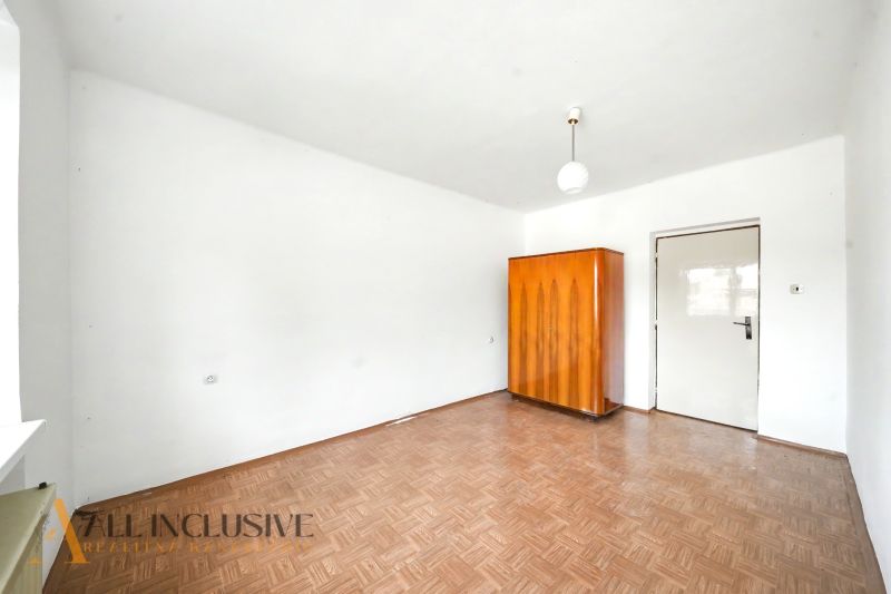 Ein Zimmer in einem Einfamilienhaus mit weißen Wänden, einem Boden in Holzoptik und einem Holzschrank.