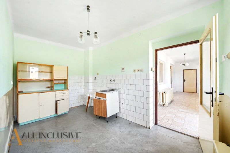 Eine Küche in einem Einfamilienhaus mit einer einfachen Küchenzeile, weißen Fliesen und einem grauen Boden.