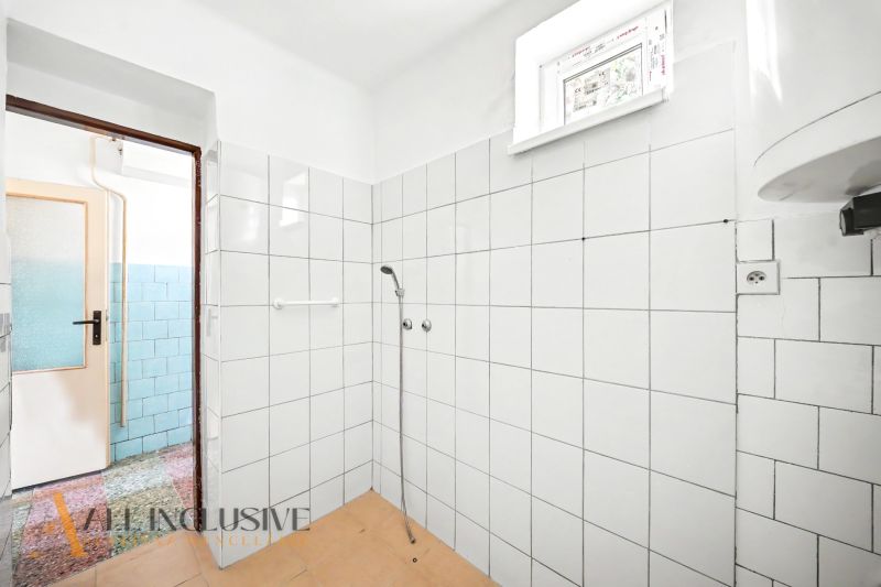 Ein Badezimmer in einem Einfamilienhaus mit weißen Fliesen und einer einfachen Dusche.