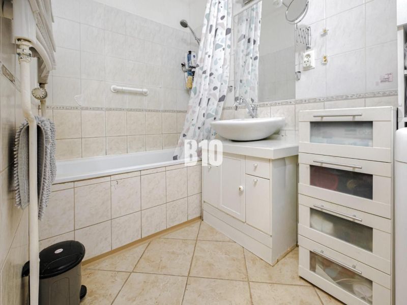 Badezimmer in einer 2-Zimmer-Wohnung mit Badewanne und weißem Waschbecken auf einem Schrank.