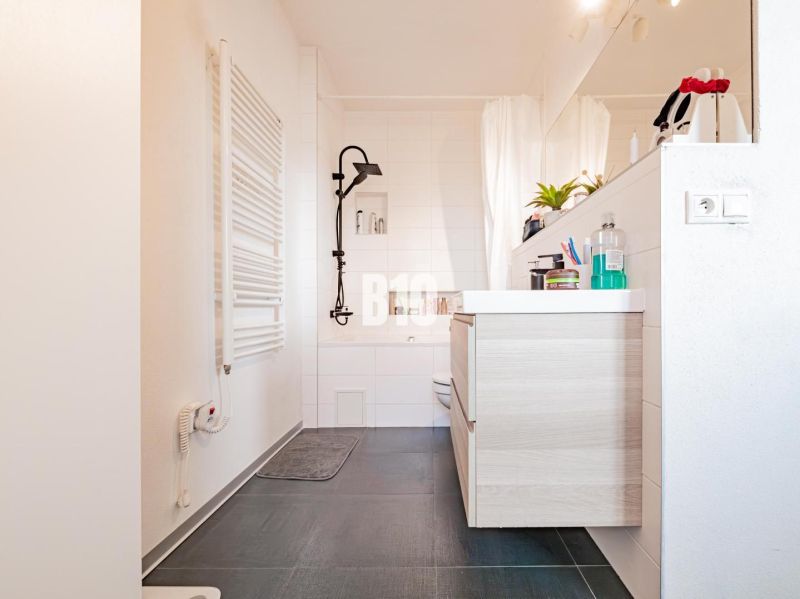 Badezimmer in einer 3-Zimmer-Wohnung mit dunklem Boden und hellen Möbeln.