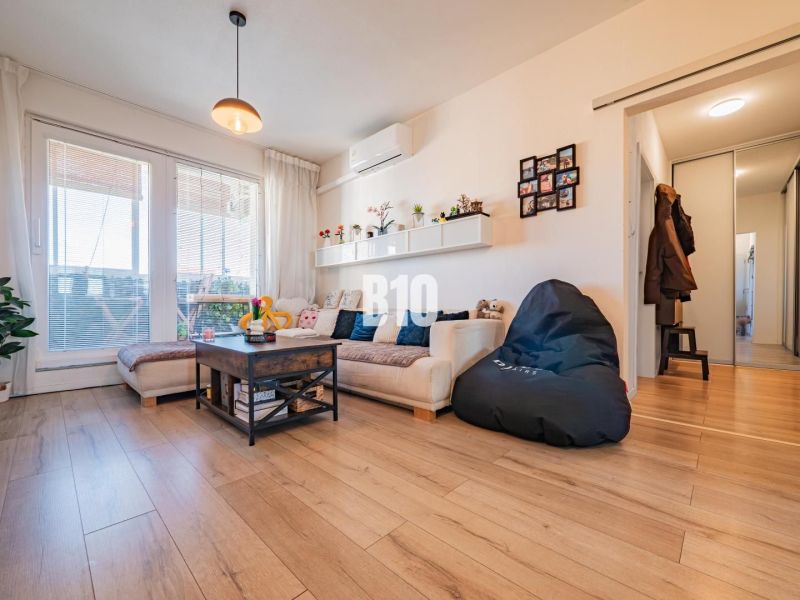 Wohnzimmer in einer 3-Zimmer-Wohnung mit Holzboden, Sofa und großen Fenstern.