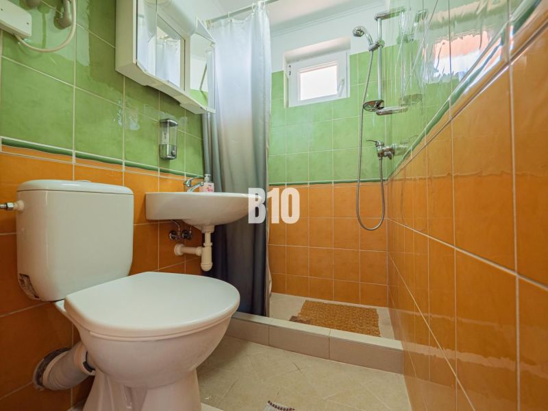 Ein Badezimmer in einem Einfamilienhaus mit orange-grünen Fliesen und einer Duschkabine.