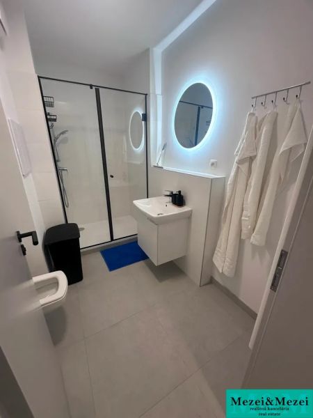 Badezimmer mit rundem Spiegel, Duschkabine und Waschbecken in einer Zweizimmerwohnung.